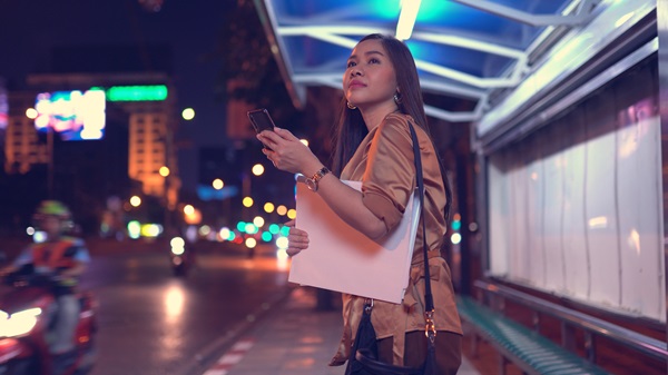 Young woman waiting for a rideshare vehicle on the side of a busy city street.