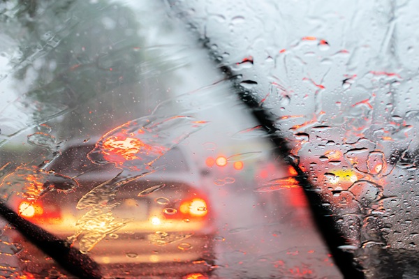 View from inside a car during heavy rain with blurred taillights and windshield wipers clearing the water.
