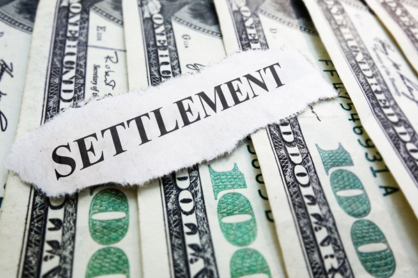 The word “Settlement” printed on a torn piece of paper placed over several one-hundred-dollar bills.