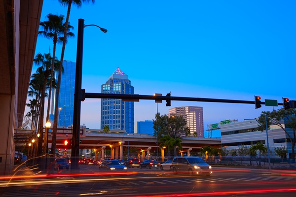 A busy intersection in downtown Tampa, Florida at dusk, with traffic streaking red light trails and palm trees lining the street.