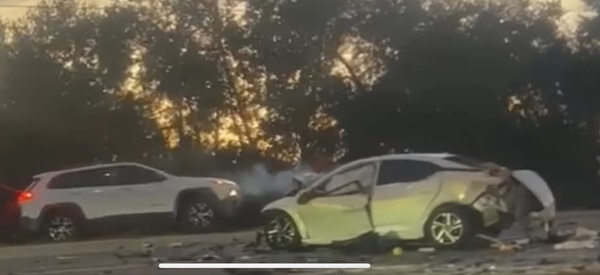 Two severely damaged vehicles, a white car and a light SUV, at the scene of a nighttime or dusk crash, with debris scattered around.