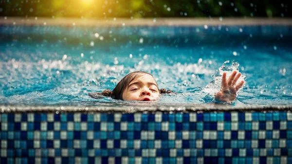 A young child with dark hair is drowning in a Florida swimming pool, their head partially submerged and one hand reaching up out of the splashing blue water.