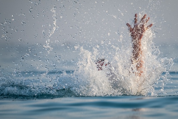 A person’s arm and hand reaching desperately out of splashing ocean water near a Florida beach as they are submerged by a wave and start to drown.