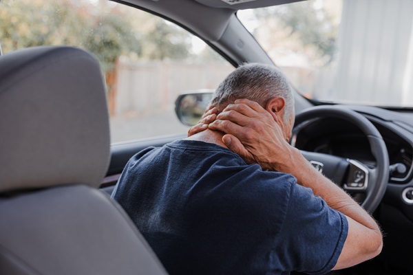 A man sitting in the driver's seat of a car gripping the back of his neck in pain, depicting a whiplash injury immediately following a motor vehicle accident in Tampa, FL.