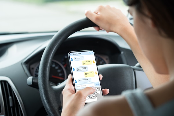 Driver texting on a cellphone while steering a vehicle, illustrating how distracted driving increases crash risk and can lead to liability in car accident cases.
